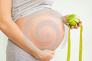A pregnant woman is holding a green apple and a centimeter in her hands. Diet during pregnancy. Proper nutrition. Weight gain