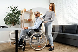 Pregnant woman holding a hand of her disabled husband sitting in a wheelchair