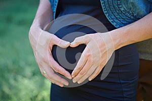 Pregnant woman holding hands on her belly in the shape of heart