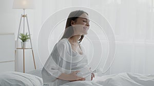 Pregnant Woman Holding Headphones Near Belly And Dancing While Sitting In Bed
