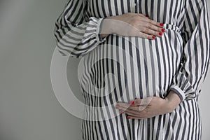 A pregnant woman holding her baby bump stood against a plain background