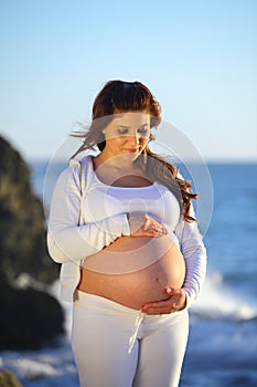 Pregnant woman holding her belly at the beach