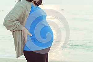 Pregnant woman holding her belly on the beach with copy space in