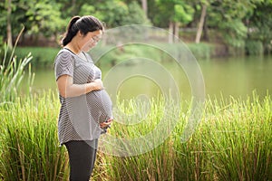 Pregnant woman holding her belly in the green gardent.