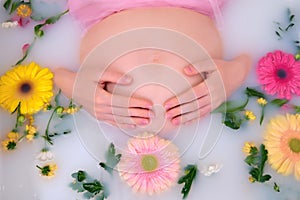 Pregnant woman holding her belly with hands in a bath with flowers