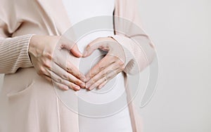 Pregnant Woman holding her hands in a heart shape on baby bump. Pregnant Belly. Maternity concept. Baby Shower