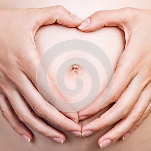 Pregnant woman holding her hands in a heart shape on belly.