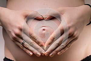 Pregnant Woman holding her hands in a heart shape on her baby bu