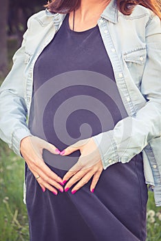 Pregnant woman holding her hands in a heart shape on her baby bump. Pregnancy, maternity and new family concept.