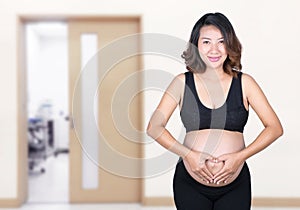 Pregnant Woman holding her hands in a heart shape on her belly i