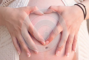 Pregnant Woman holding her hands in a heart shape on her belly; maternity and family concept