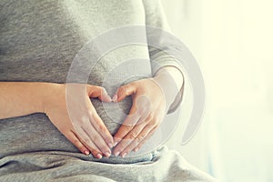 Pregnant woman holding her hands on her swollen belly shaping a