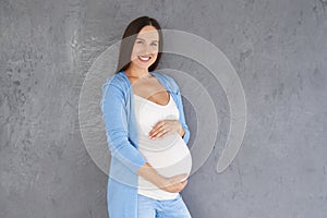 Pregnant woman holding her tummy against grey background