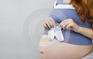 Pregnant woman holding little baby socks on belly on  grey background