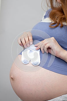 Pregnant woman holding little baby socks on belly on isolated grey background