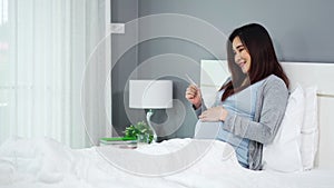 Pregnant woman holding and looking ultrasound scan photo on a bed
