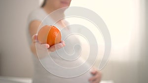 Pregnant woman is holding an orange in her hand. The concept of healthy eating during pregnancy.