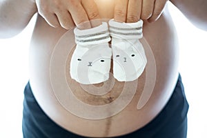 Pregnant woman holding a pair of cute baby socks on her bare tummy