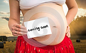 Pregnant woman holding paper with inscription: coming soon