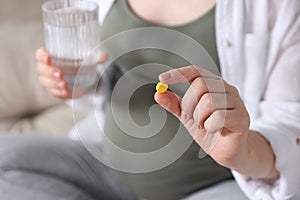 Pregnant woman holding pill and glass of water on blurred background, closeup