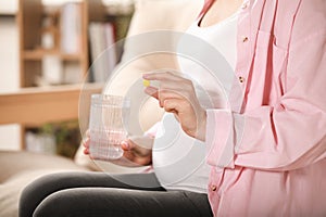Pregnant woman holding pill and glass with water at home, closeup