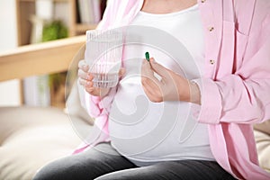 Pregnant woman holding pill and glass of water at home, closeup