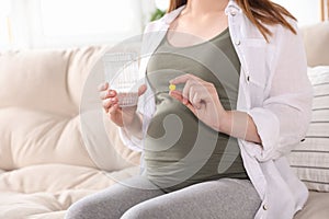 Pregnant woman holding pill and glass with water at home, closeup