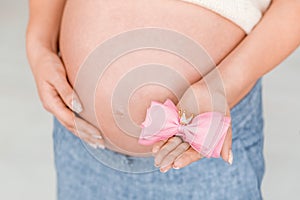 Pregnant woman is holding a pink bow with a golden crown on her belly waiting for child& x27;s birth. Gender reveal