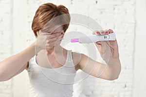 Pregnant woman holding pink positive pregnancy test covering her eyes with her hand
