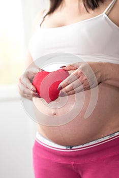 Pregnant woman holding a red heart on her belly