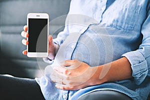 Pregnant woman holding and showing mobile phone with empty display.