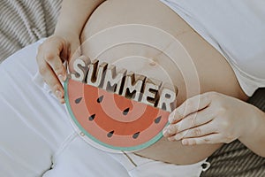 A pregnant woman is holding a slice of watermelon.