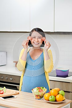 Pregnant woman holding sliced tomato and covering eyes, concept of healthy food and nutrition during pregnancy