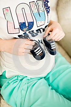 Pregnant woman holding small baby shoes