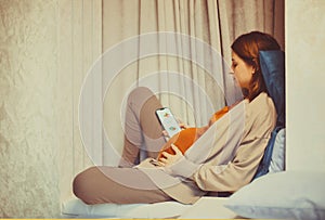 Pregnant woman holding smartphone using pregnancy tracker app on mobile phone while sitting indoors