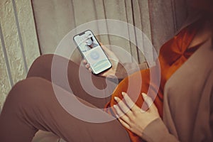 Pregnant woman holding smartphone using pregnancy tracker app on mobile phone while sitting indoors