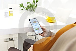 Pregnant woman holding smartphone using pregnancy tracker app on mobile phone while sitting indoors