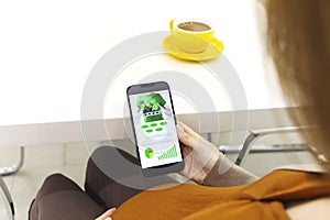 Pregnant woman holding smartphone using pregnancy tracker app on mobile phone while sitting indoors