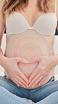 Pregnant woman holding stomach in heart shape gesture with hands on her belly. Pregnancy concept photoshoot