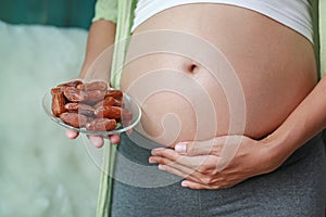 Pregnant woman holding Sweet dried Date Palm fruit at her belly. Dieting Concept. Healthy Lifestyle