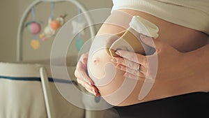 Pregnant woman holding tiny baby socks over her belly. Baby crib with spinning toys in the backgournd. Expecting and