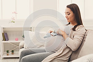 Pregnant woman holding tiny shoes near belly