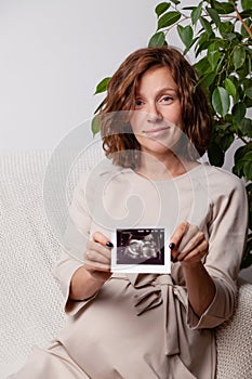 Pregnant woman holding ultrasound image. Concept of pregnancy, health care, gynecology, medicine. Young mother waiting