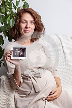 Pregnant woman holding ultrasound image. Concept of pregnancy, health care, gynecology, medicine. Young mother waiting