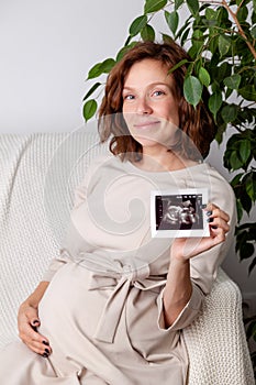 Pregnant woman holding ultrasound image. Concept of pregnancy, health care, gynecology, medicine. Young mother waiting