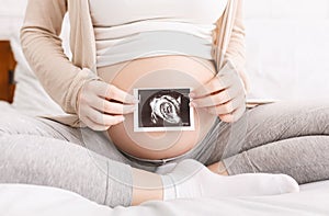 Pregnant woman holding ultrasound photo near belly