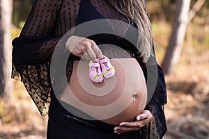 Pregnant woman holding unborn baby girl`s shoes