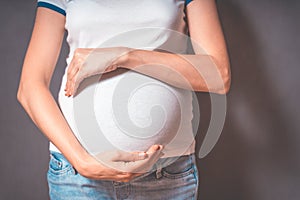 Pregnant woman holds hands on belly on a gray background.