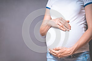 Pregnant woman holds hands on belly on a gray background.