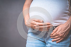 Pregnant woman holds hands on belly on a gray background.